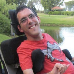 Image of Ben, a man who uses an electric wheelchair, in a park in front of a lake